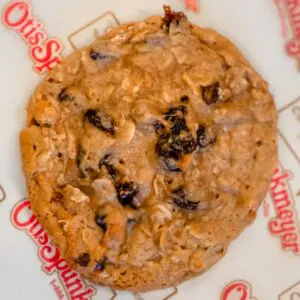 A close-up of an oatmeal raisin cookie on Otis Spunkmeyer branded paper.