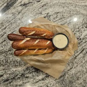 Four pretzel sticks with salt and a side of dipping sauce in a paper-lined basket.