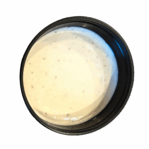 A black plastic container filled with creamy white ranch dressing, viewed from above.